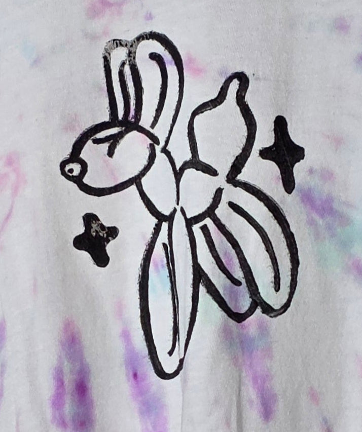 Tie-dye t-shirt with a black balloon animal design on a hanger against a patterned wall.