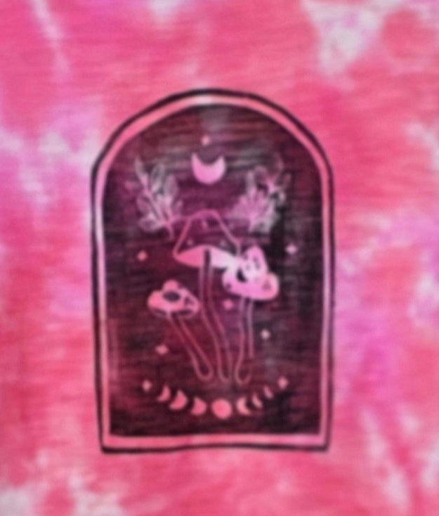 Pink and white tie-dye t-shirt with a graphic patch on a hanger against a patterned wall.