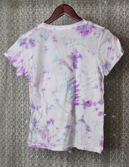 Short-sleeve shirt with a tie dye pattern on a hanger against a textured wall.