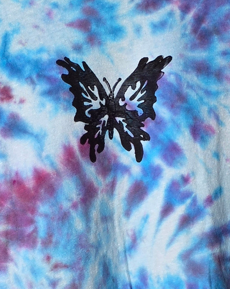 Tie-dye t-shirt with a butterfly design on a hanger against a patterned wall.