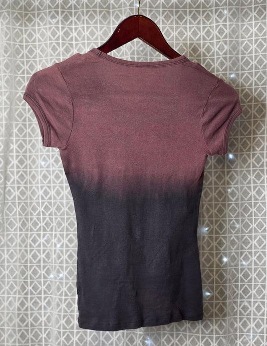 Ombre t-shirt with gradient from purple to black on a hanger against a patterned wall.