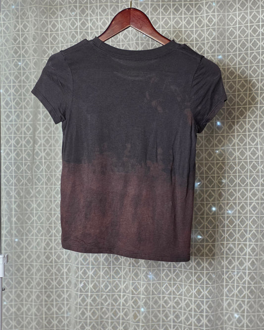 Black t-shirt with gradient effect on a hanger against a patterned wall.