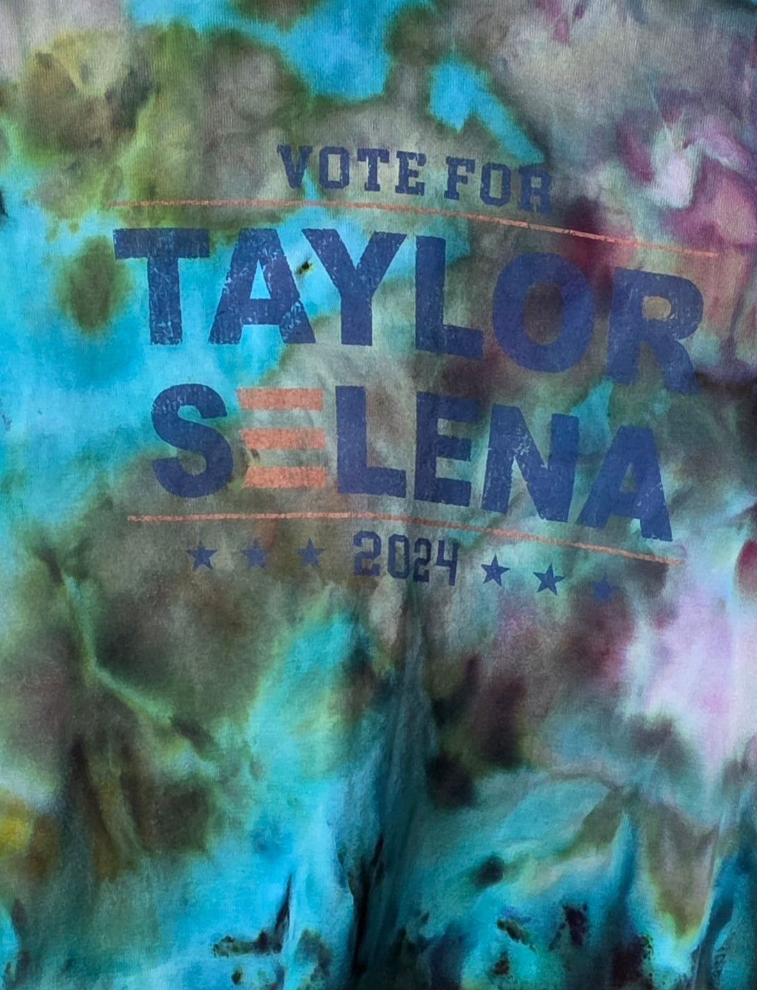 Tie-dye t-shirt with text on a hanger against a patterned wall