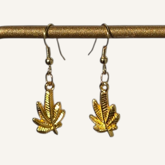 Gold leaf-shaped earrings hanging from a brass rod on a white background