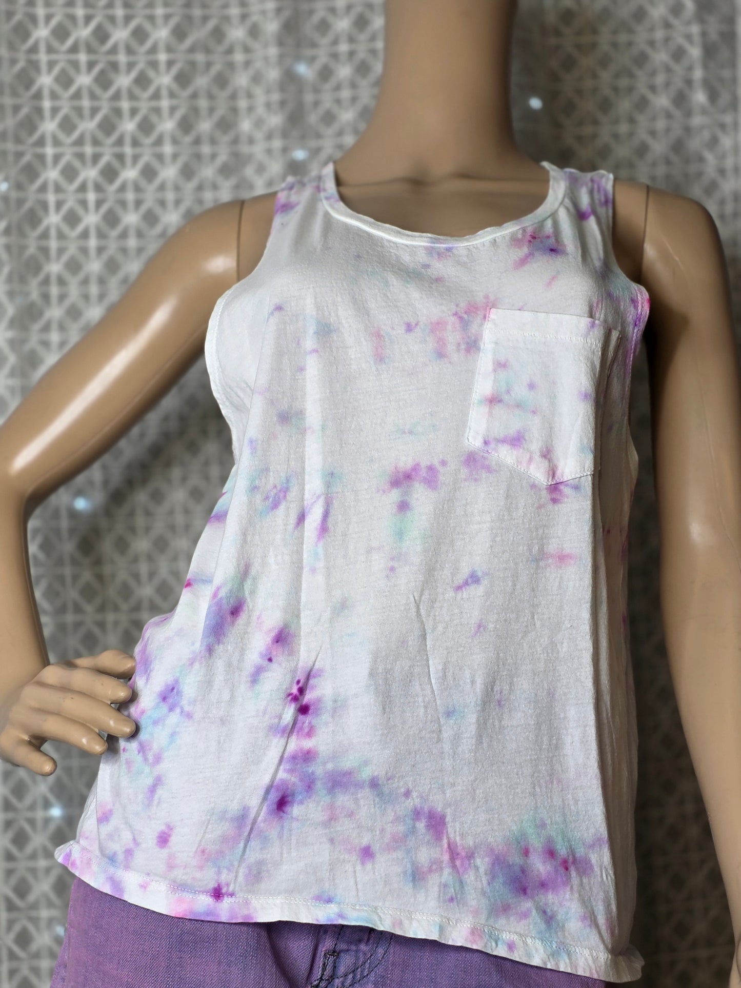 Mannequin wearing a white tank top with purple tie dye patterns on a textured surface.