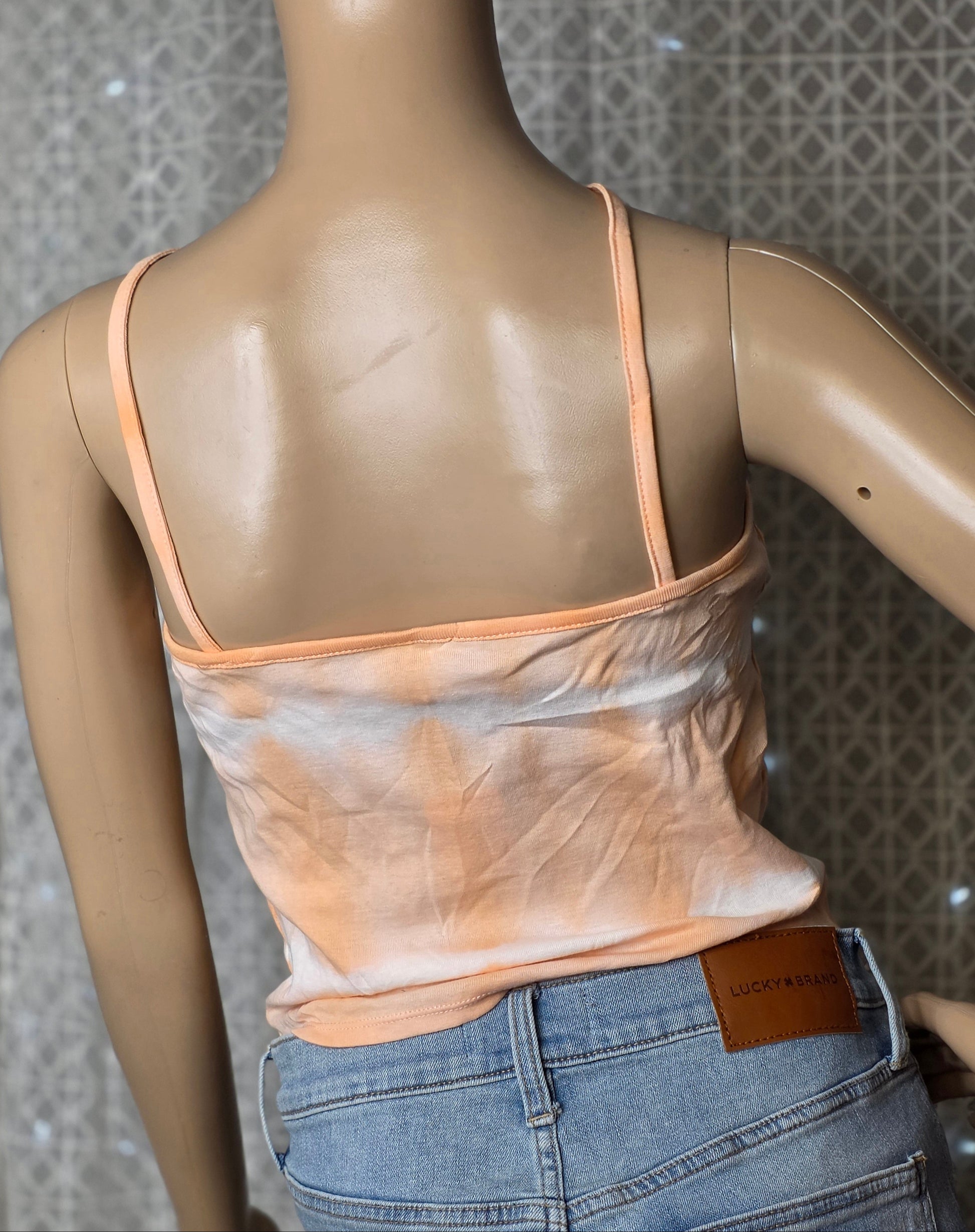 Mannequin wearing a peach tank top and blue jeans with a patterned wall background