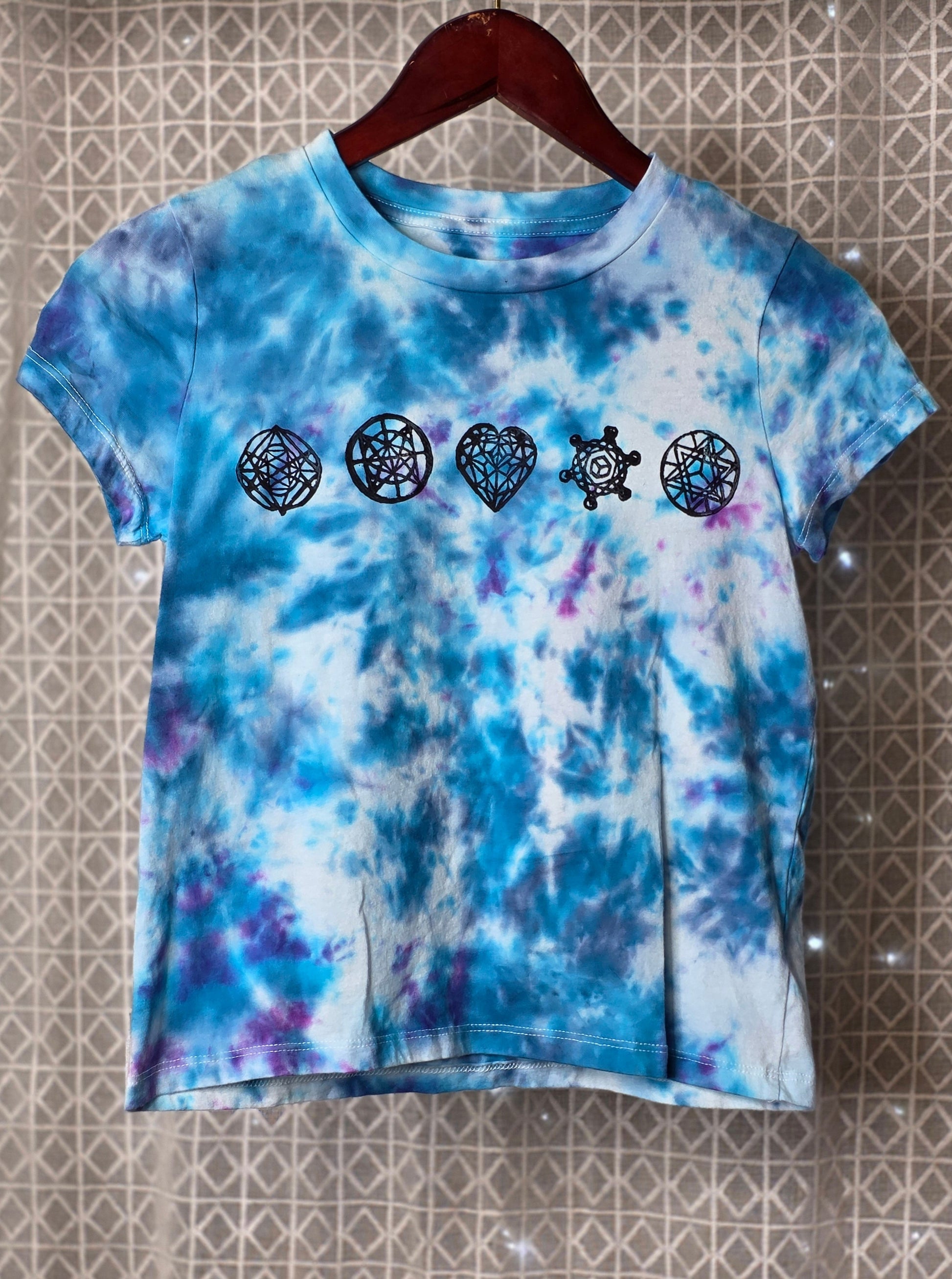 Tie-dye t-shirt with black sacred geometry symbols on a textured wall background