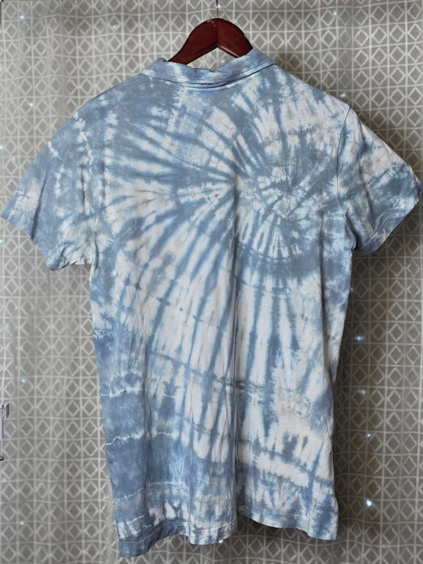Tie-dye shirt on a hanger against a patterned wall