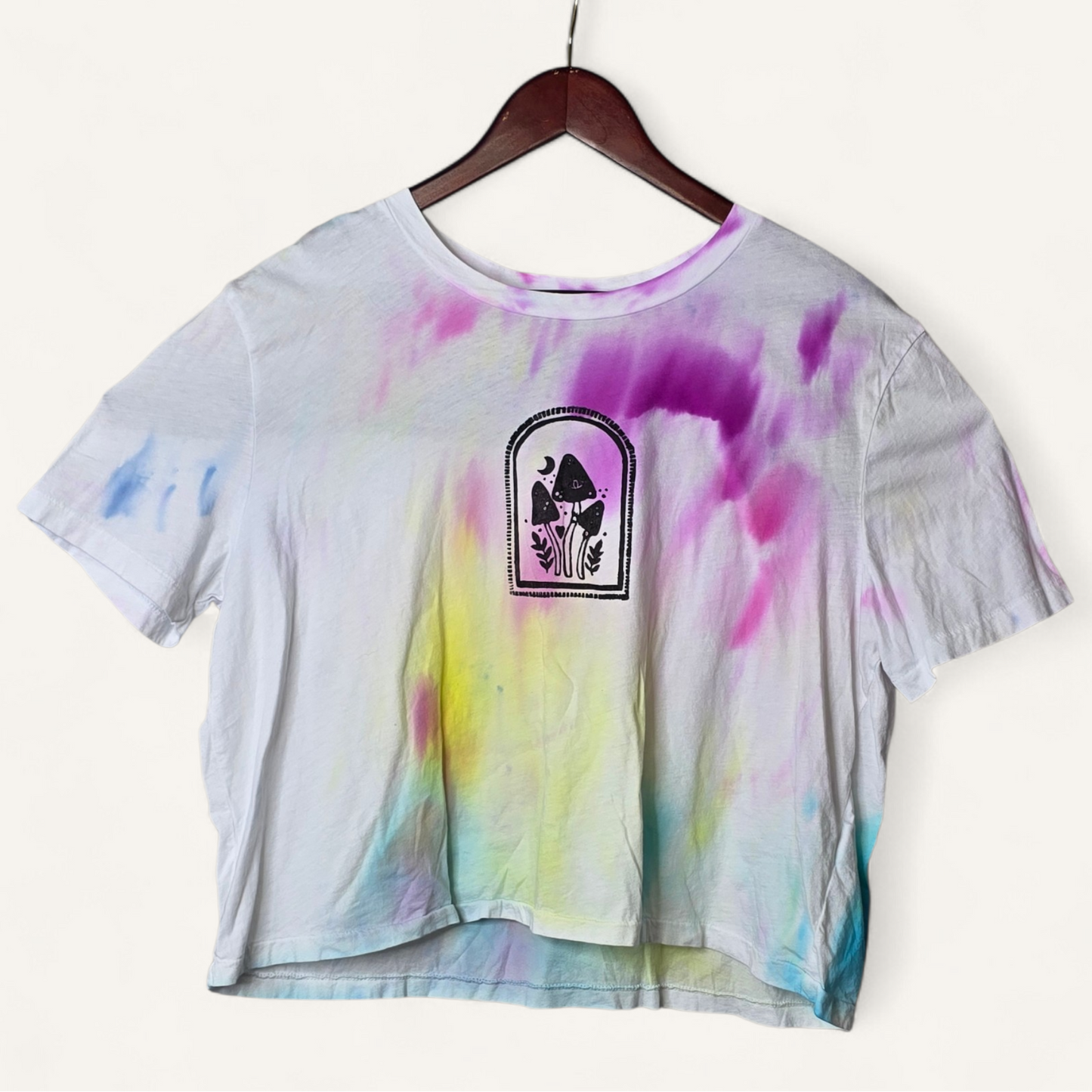Tie-dye t-shirt with a logo on a hanger against a white background