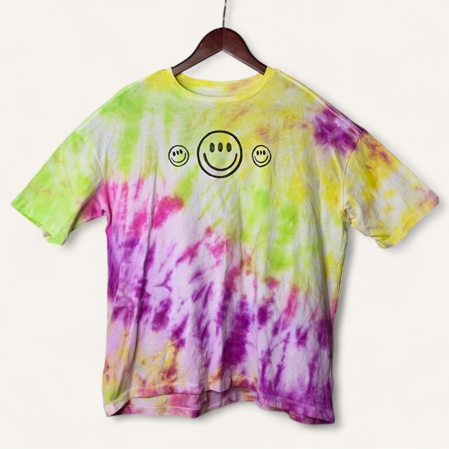 Tie-dye t-shirt with smiley face design on a hanger against a white background