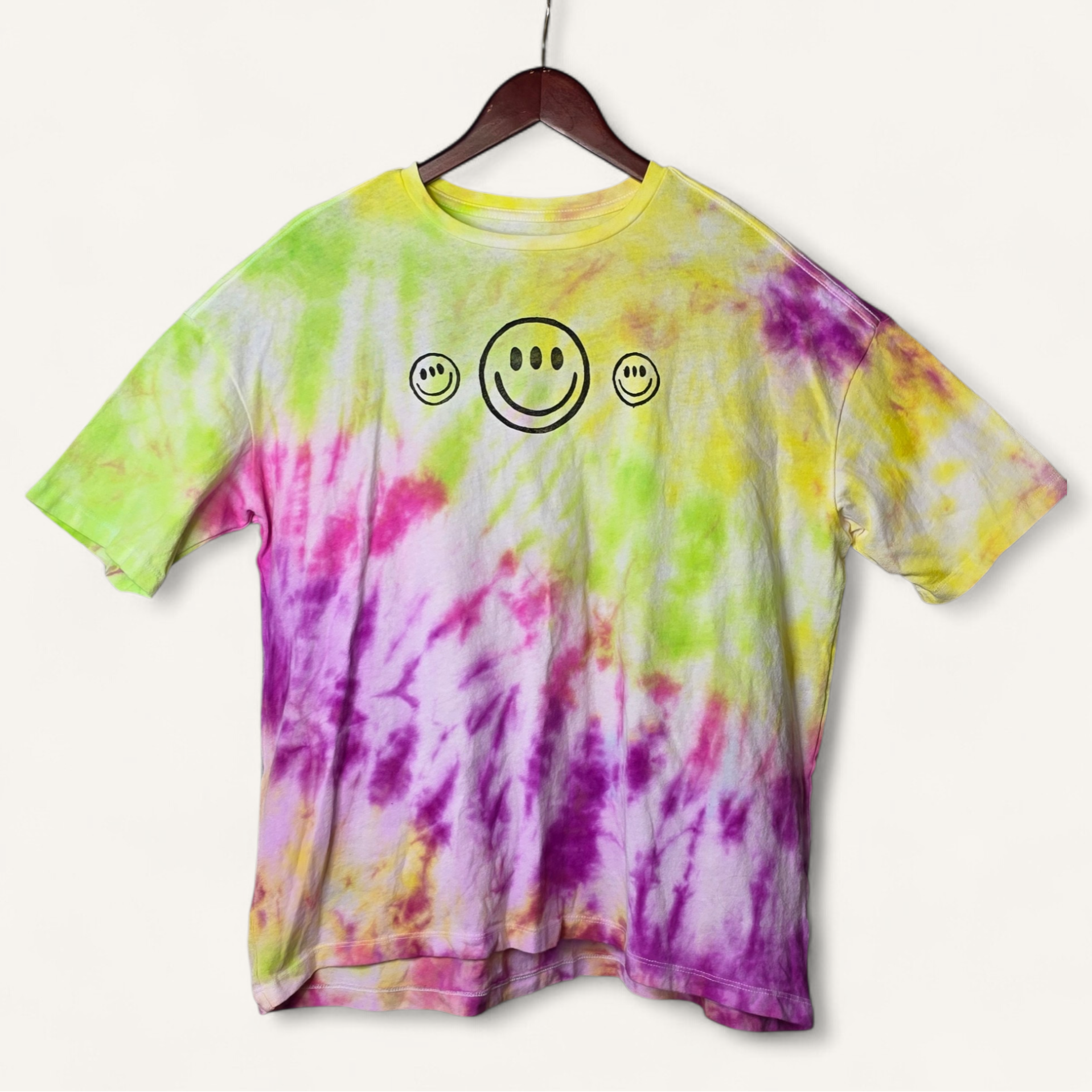Tie-dye t-shirt with smiley face design on a hanger against a white background
