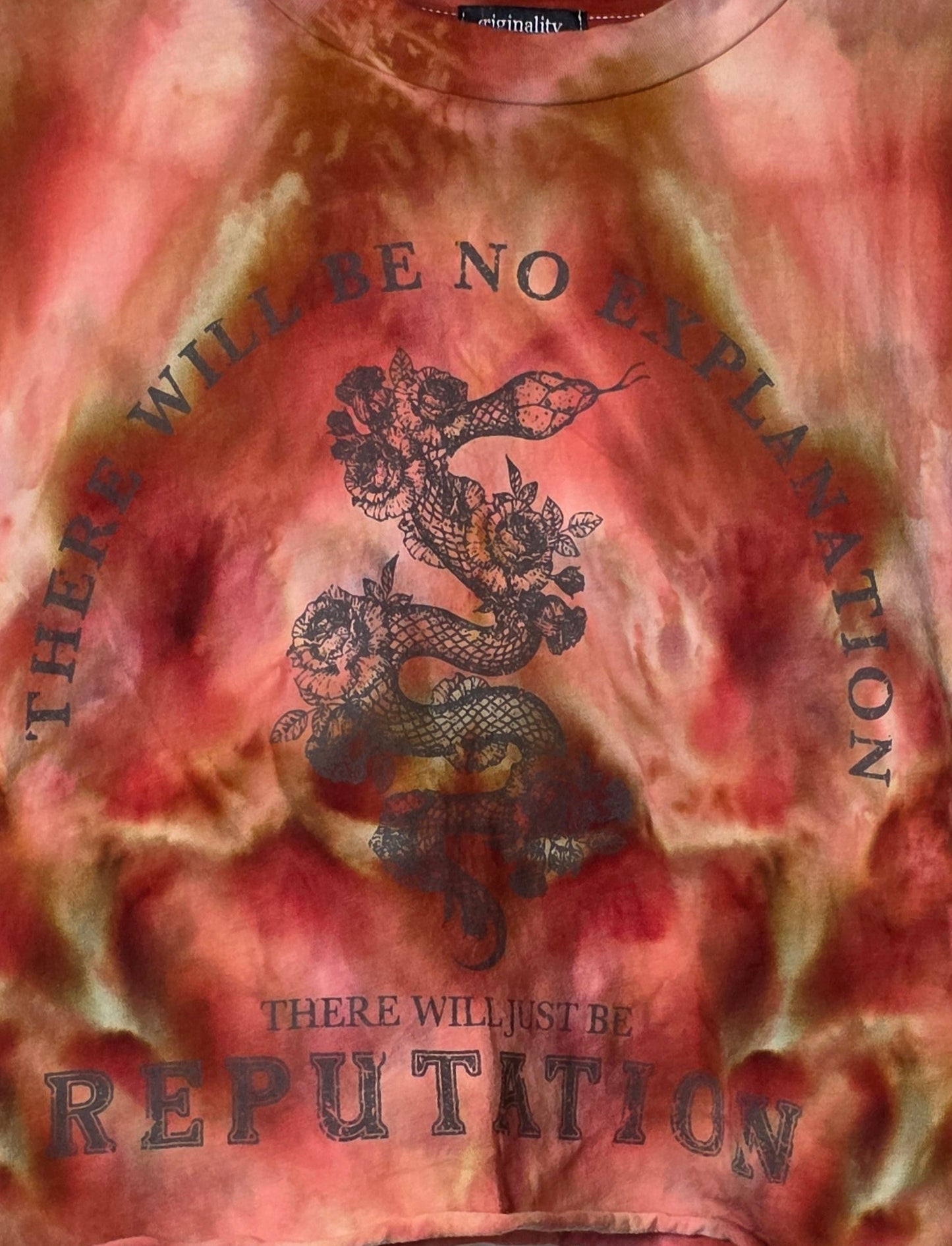 Tie-dye t-shirt with text and graphic design on a hanger against a patterned wall.