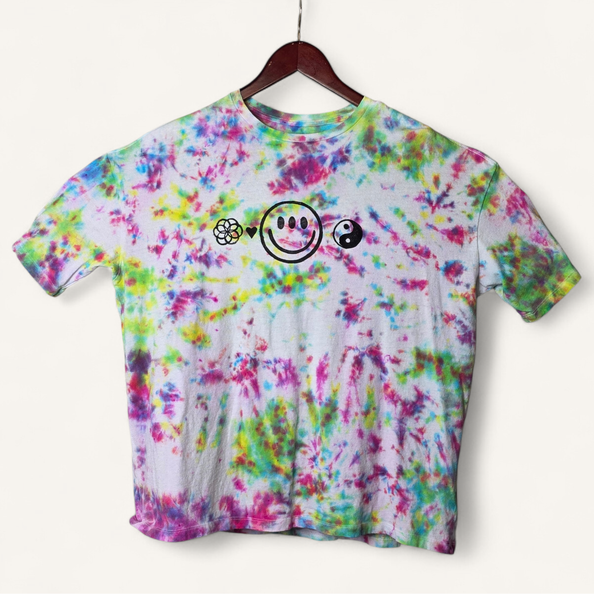 Colorful tie-dye t-shirt with smiley face design on a hanger against a white background
