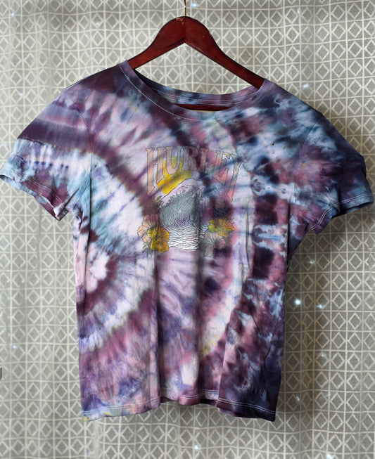 Tie-dye t-shirt with graphic design on a hanger against a patterned wall.