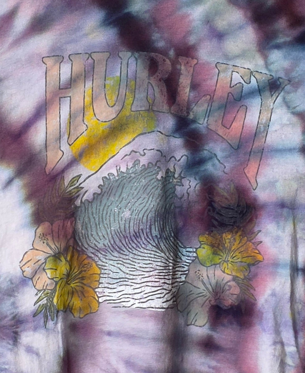 Tie-dye t-shirt with graphic design on a hanger against a patterned wall.