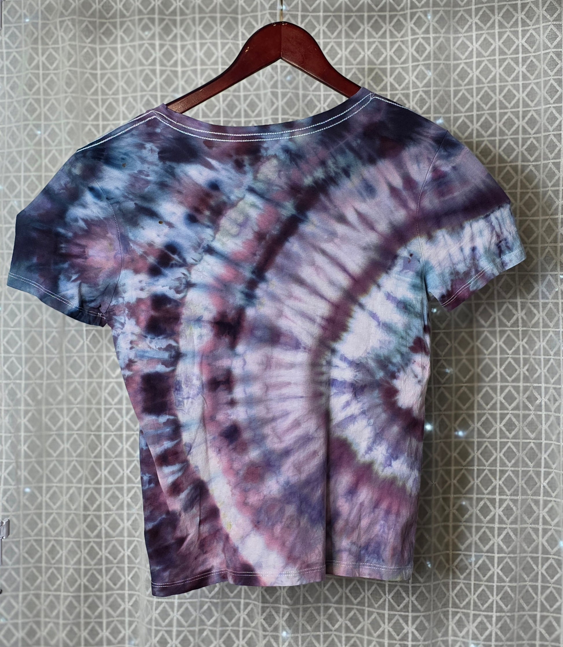 Tie-dye t-shirt on a hanger against a patterned wall.