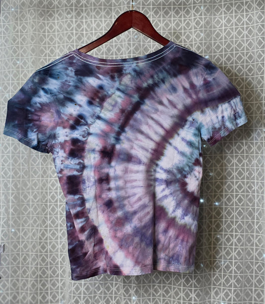 Tie-dye t-shirt on a hanger against a patterned wall.