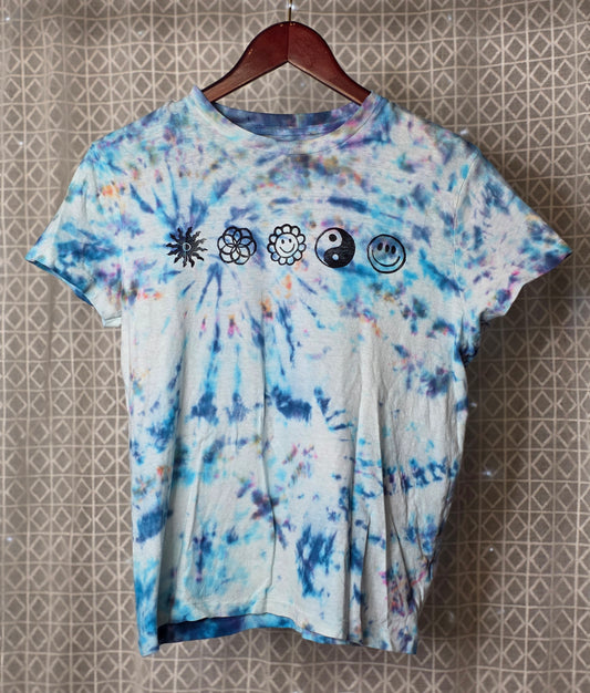 Tie-dye t-shirt with symbols on a hanger against a patterned wall.