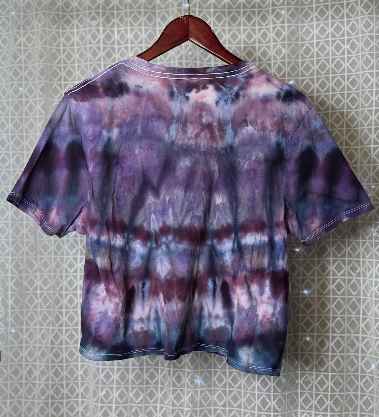 Tie-dye t-shirt on a hanger against a patterned wall.