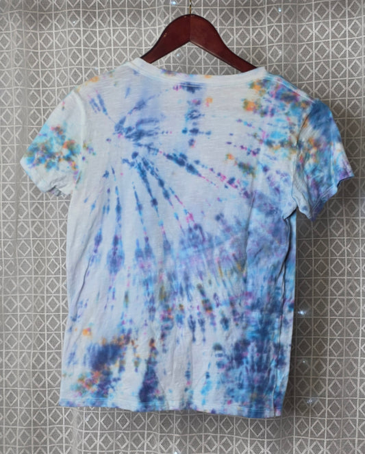 Tie-dye t-shirt on a hanger against a patterned wall.