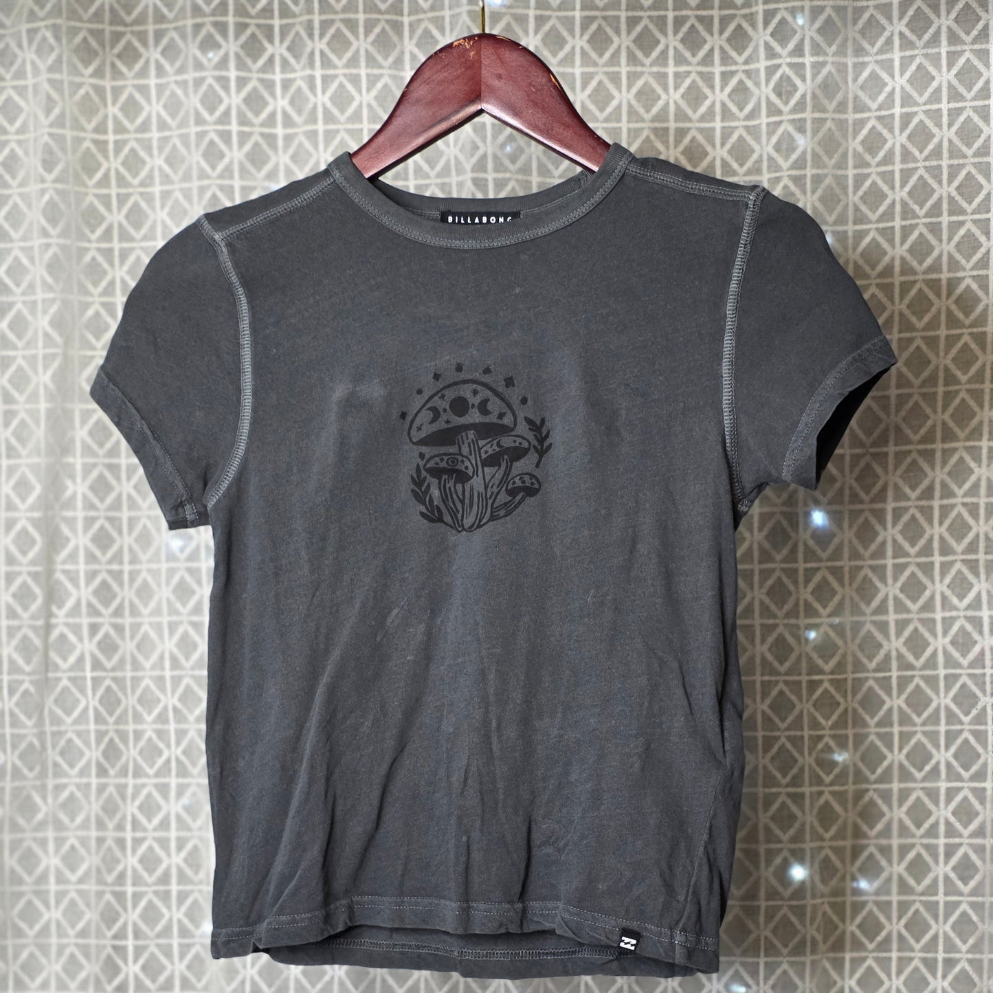 Gray t-shirt with a mushroom print on a hanger against a patterned wall
