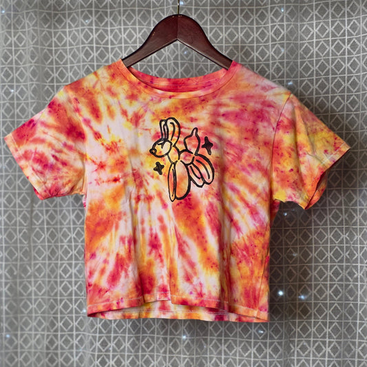 Tie-dye t-shirt with a balloon animal print on a hanger against a patterned wall.
