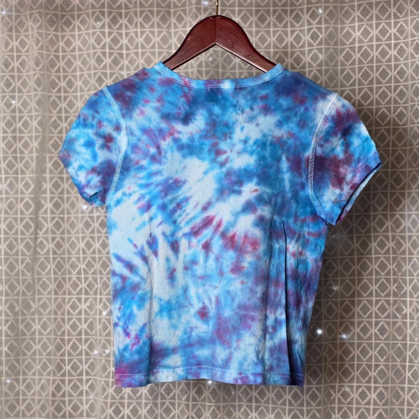 Tie-dye t-shirt on a hanger against a patterned wall