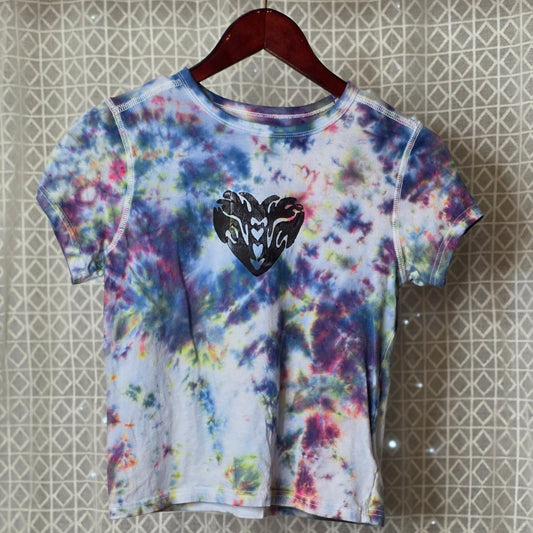 Colorful tie-dye t-shirt with a black heartcon a hanger against a patterned wall.