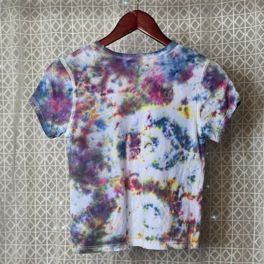 Colorful tie-dye t-shirt on a hanger against a patterned wall.
