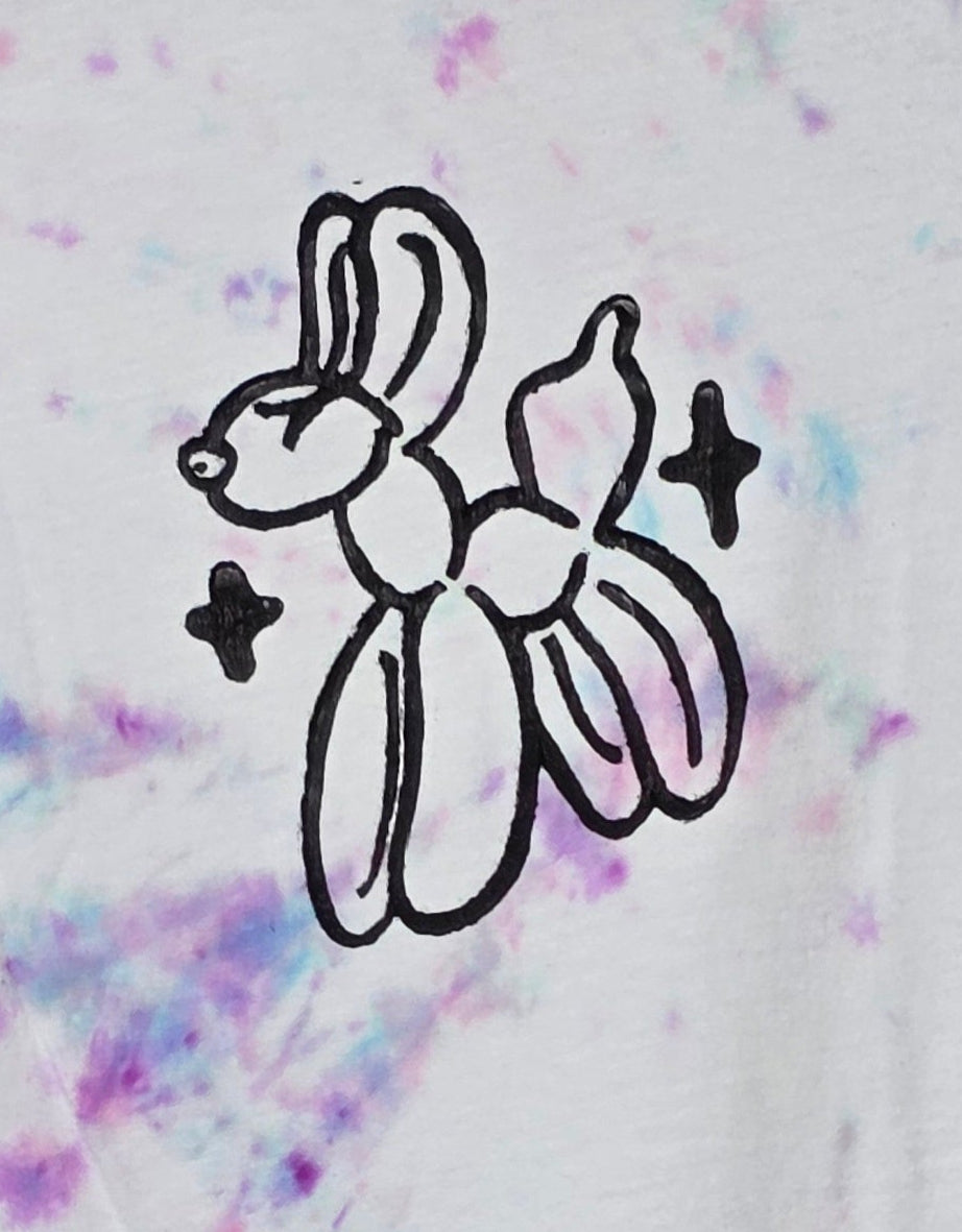 Tie-dye t-shirt with a black graphic design on a hanger against a patterned wall.