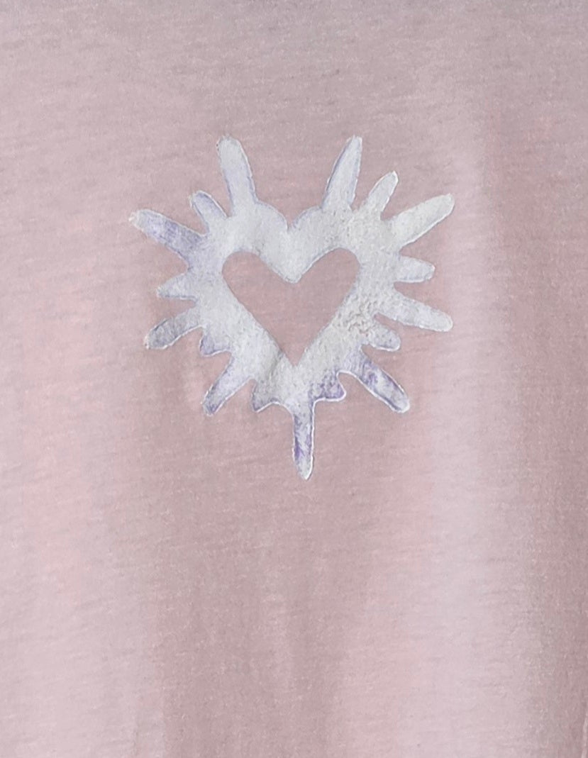 Pink t-shirt with a white heart design on a hanger against a patterned wall.