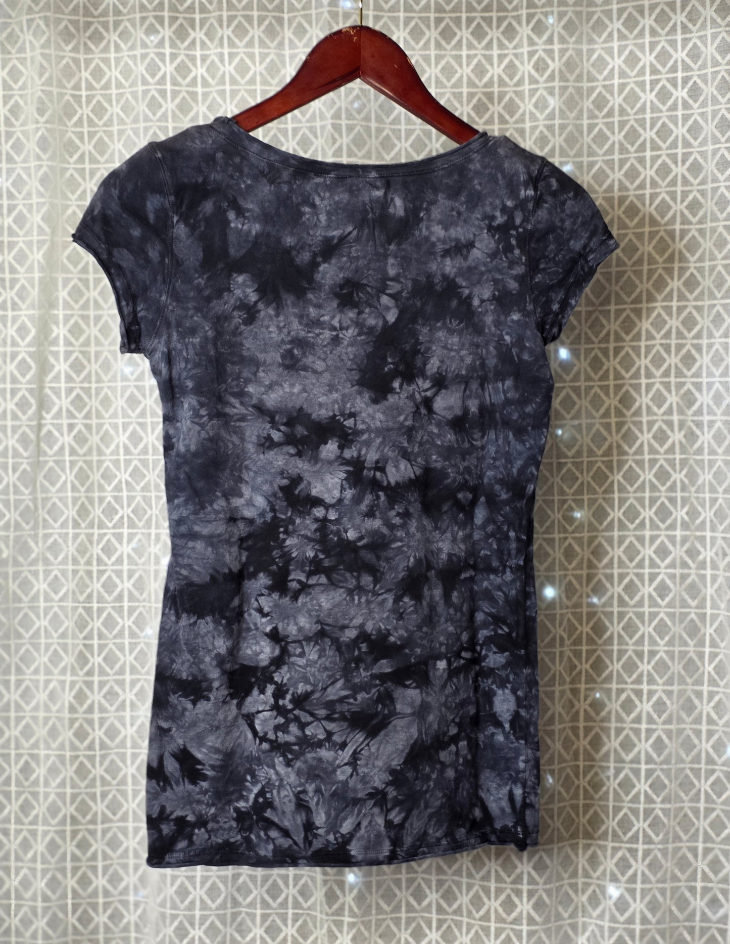 Black tie-dye dress on a hanger against a patterned wall