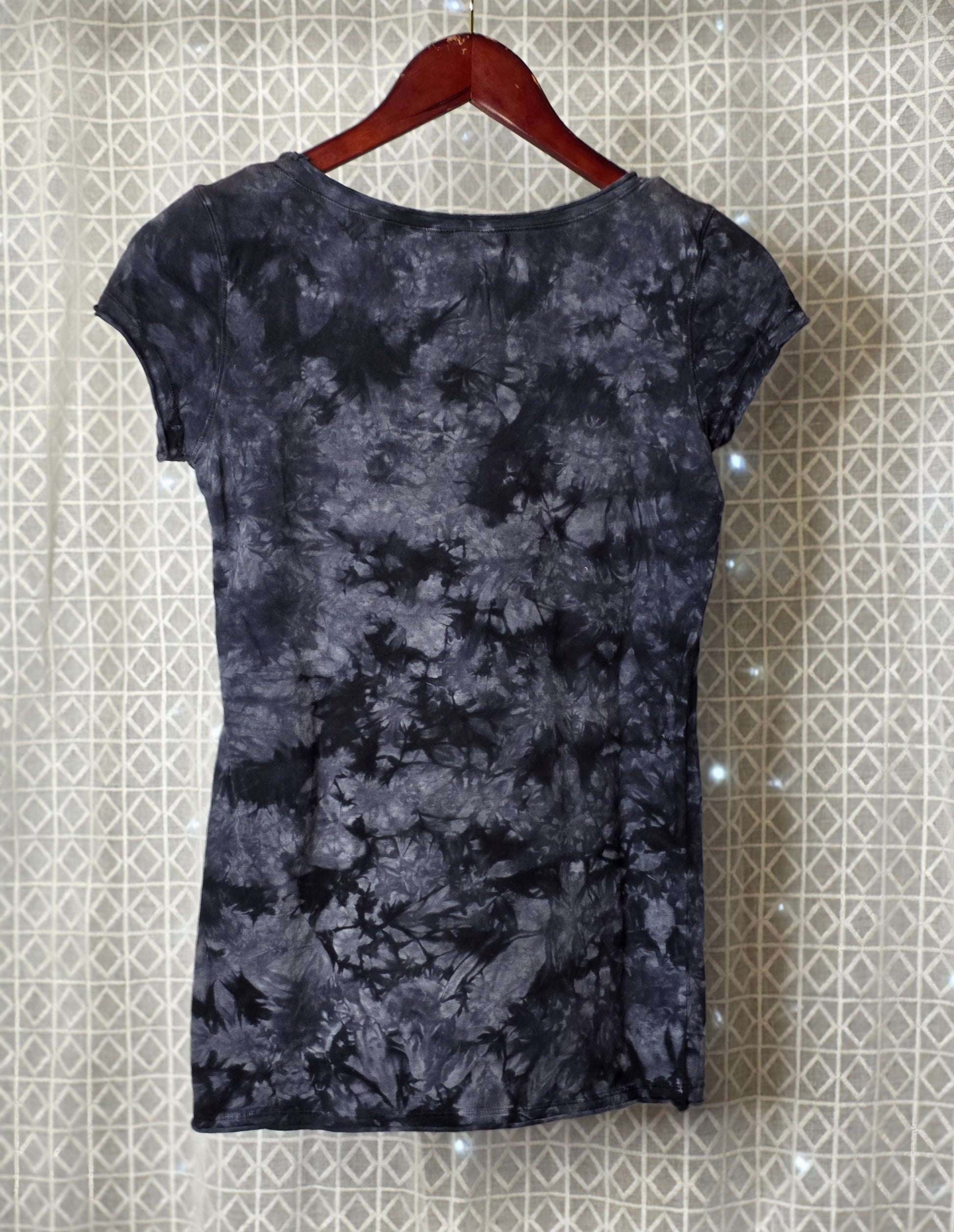 Black tie-dye dress on a hanger against a patterned wall