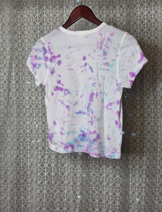 T-shirt with a smiley face design on a hanger against a patterned wall.