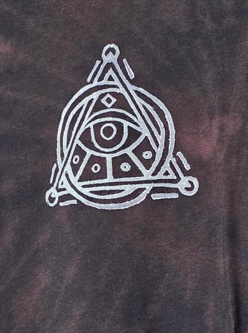 Tie-dye t-shirt with a white symbol on a hanger against a patterned wall.
