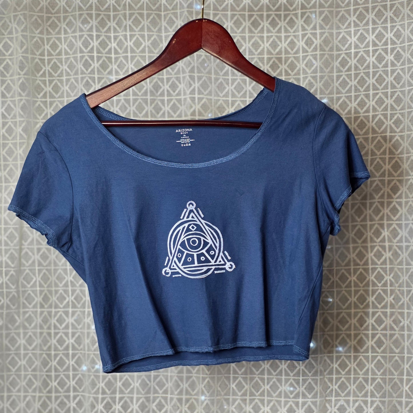 Blue t-shirt with a white logo on a hanger against a patterned wall.