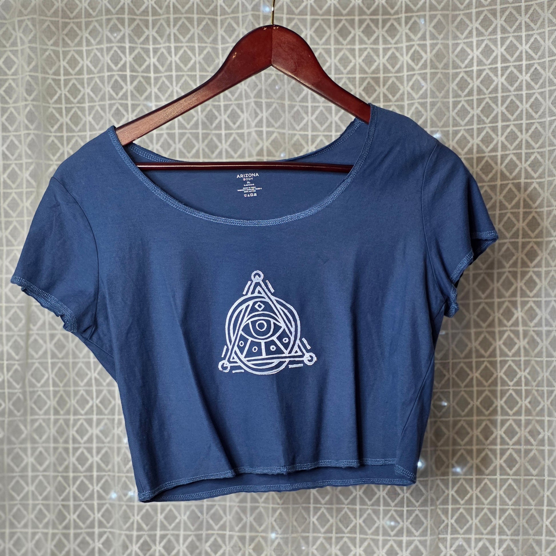 Blue t-shirt with a white logo on a hanger against a patterned wall.