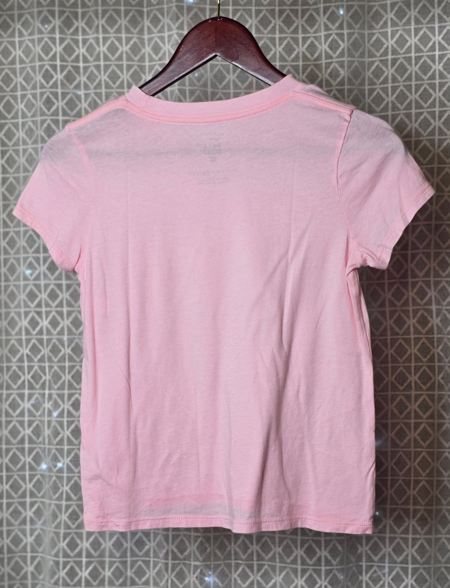 Pink t-shirt on a hanger against a patterned wall