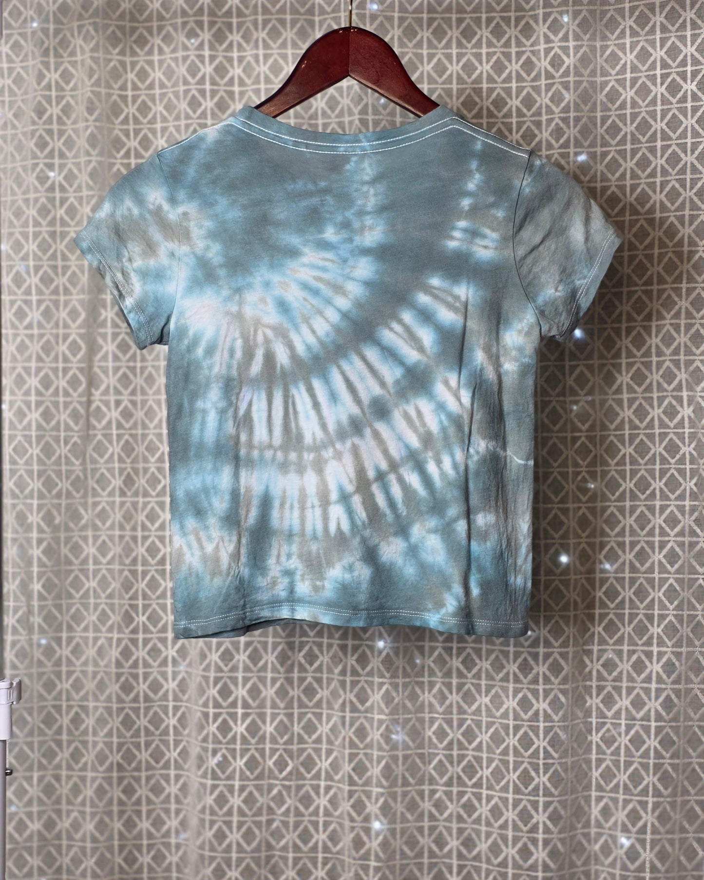 Tie-dye t-shirt on a hanger against a patterned wall