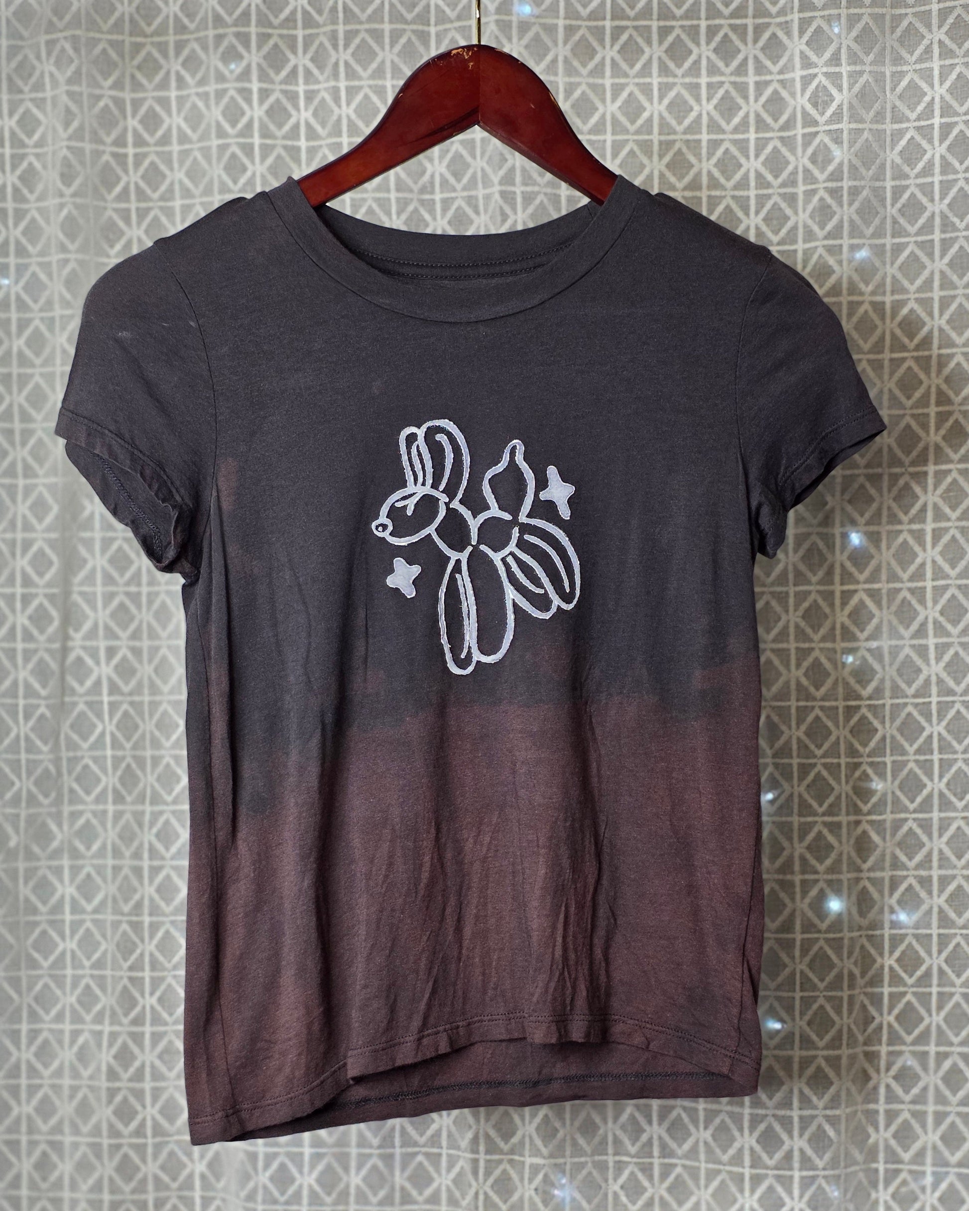 Black t-shirt with a white balloon animal graphic on a hanger against a patterned wall.