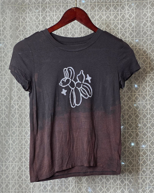 Black t-shirt with a white balloon animal graphic on a hanger against a patterned wall.