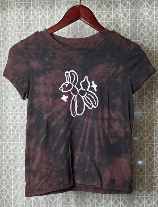 Tie-dye t-shirt with a white balloon animal graphic on a hanger against a patterned wall.