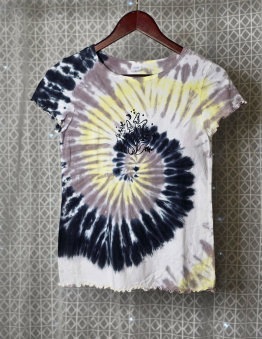 Tie-dye t-shirt with a spiral design on a hanger against a patterned wall.