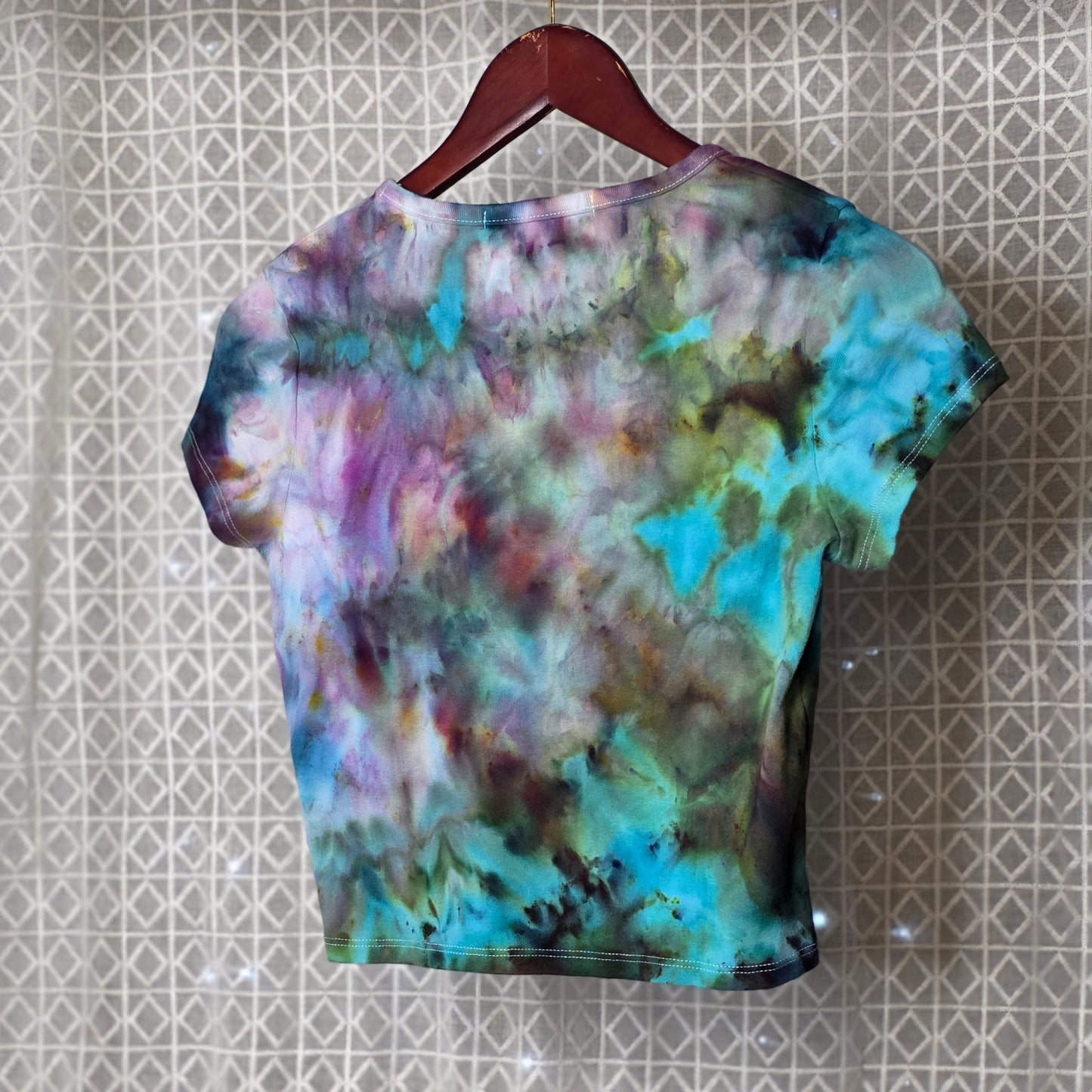 Colorful tie-dye t-shirt on a hanger against a patterned wall.