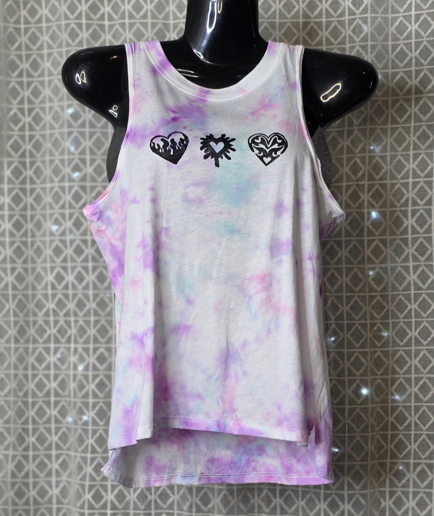 Tie-dye tank top with heart designs on a mannequin against a patterned background