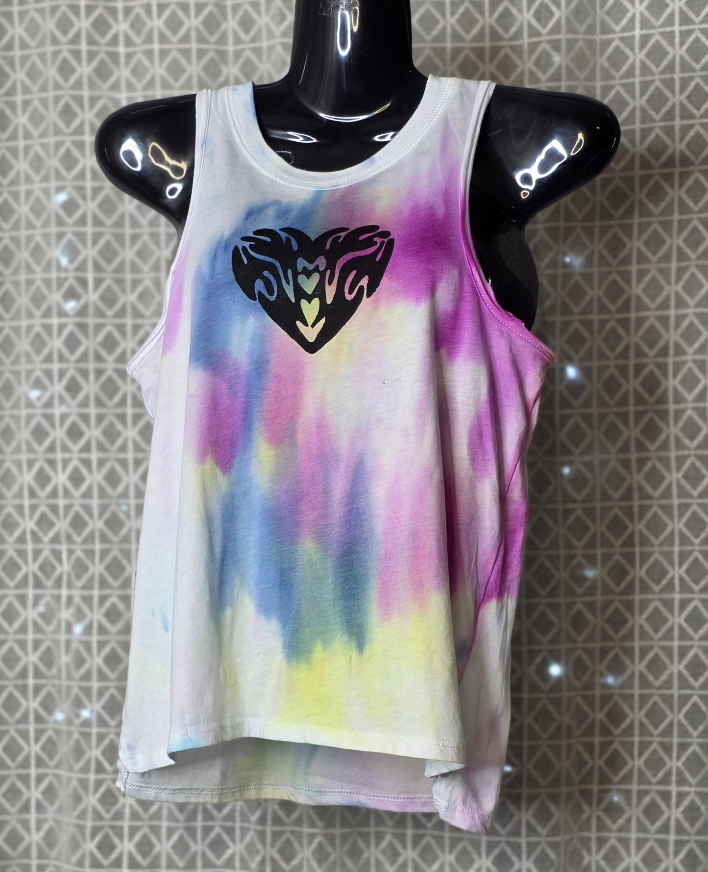 Tie-dye tank top with a black heart design on a mannequin against a patterned wall.