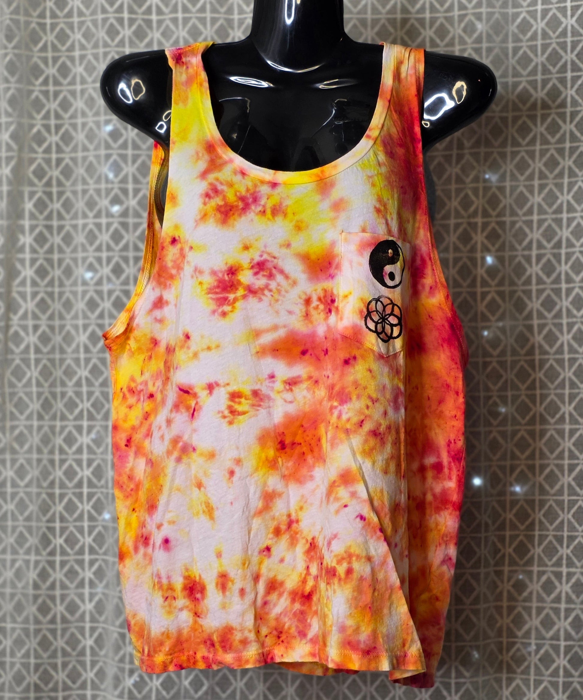 Tie-dye tank top with a design on a mannequin against a patterned wall.