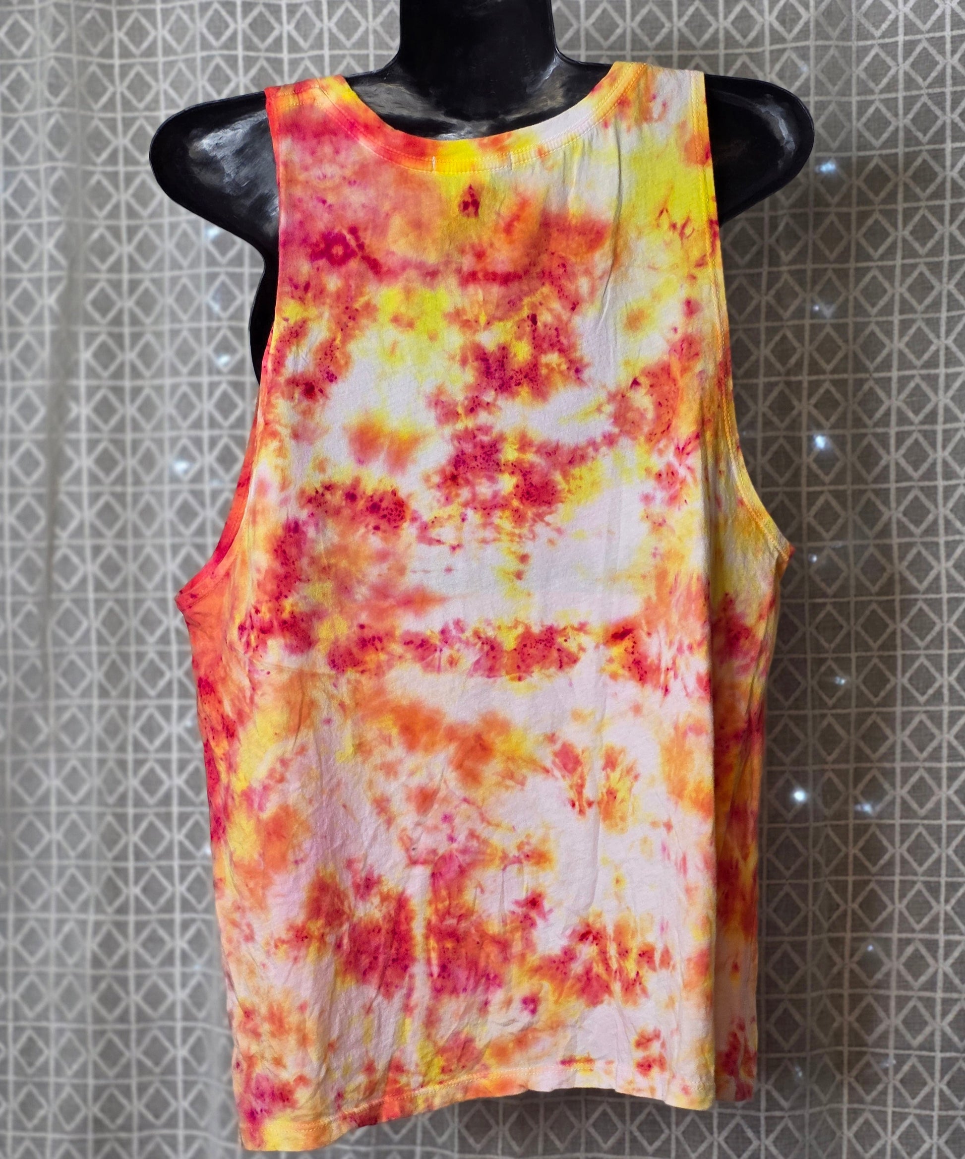Colorful tie-dye sleeveless top on a mannequin against a patterned wall.