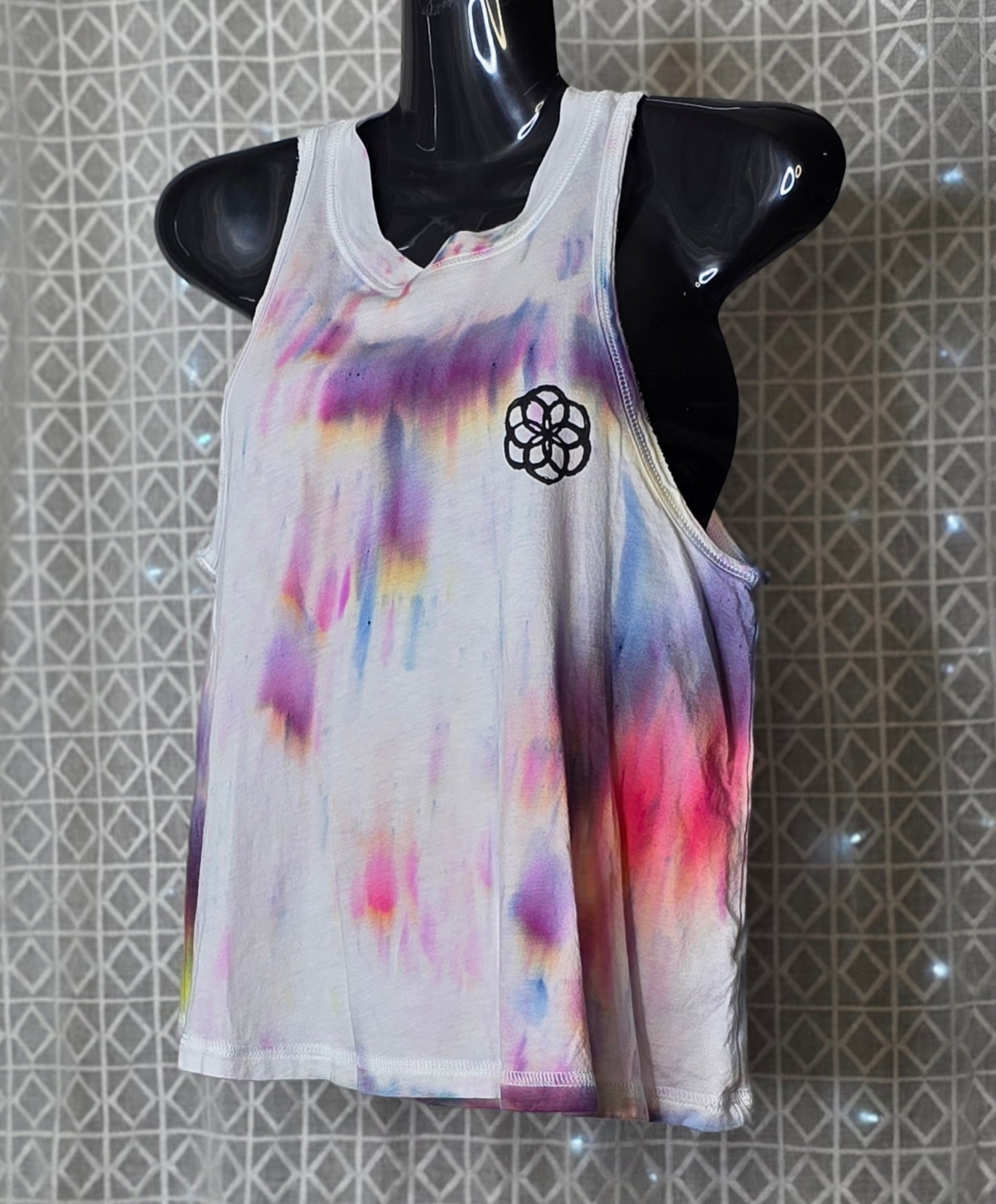 Colorful tie-dye tank top with a black symbol on a mannequin against a patterned wall.