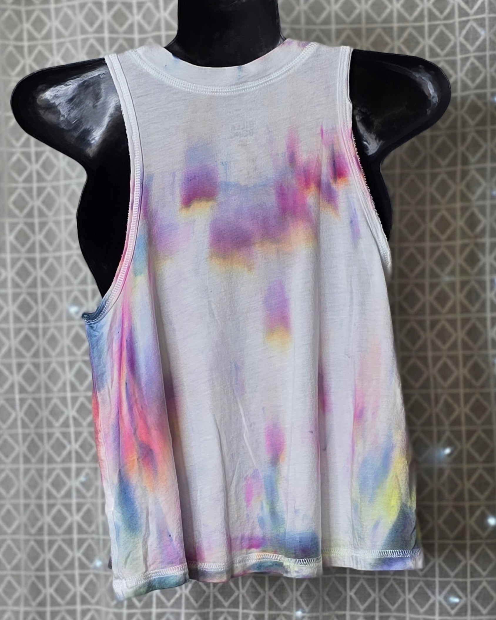 Tie-dye tank top on a mannequin against a patterned wall.